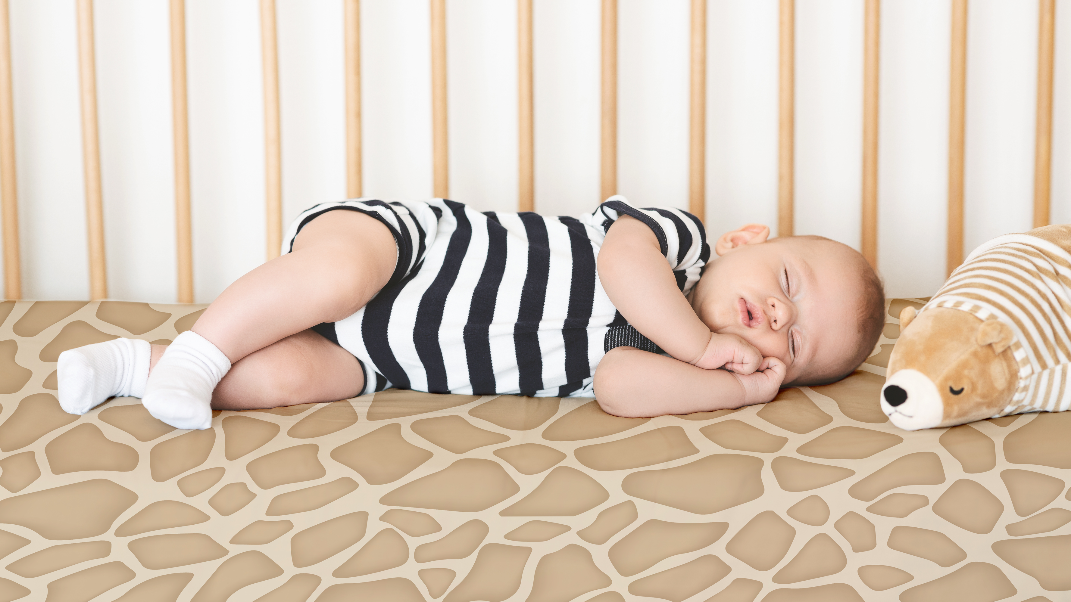 baby sleeping in a crib on a giraffe patterned crib sheet